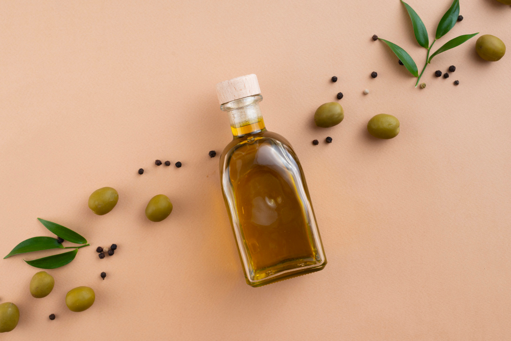 Botella de aceite de oliva rodeada con aceitunas y hojitas de olivo organizadas en forma ordenada sobre un fondo en tono neutro.
