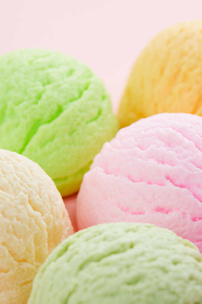 Close up de 5 bolas de helado de diferentes sabores y colores, sobre un fondo rosa pastel.