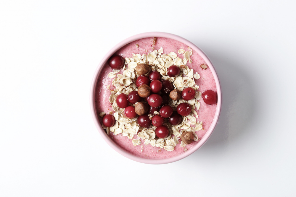 Vista cenital de un smoothie bowl que contiene un batido en color rosa coronado con almendras laminadas, cerezas y avellanas.